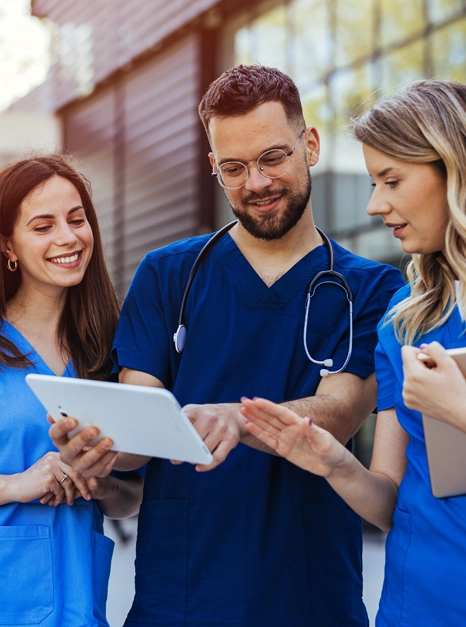 Drei Pflege- und Assistenzkräfte in blauer Dienstkleidung besprechen sich mit Tablet – qualifiziertes Team von 24h Assistance Care Hamburg